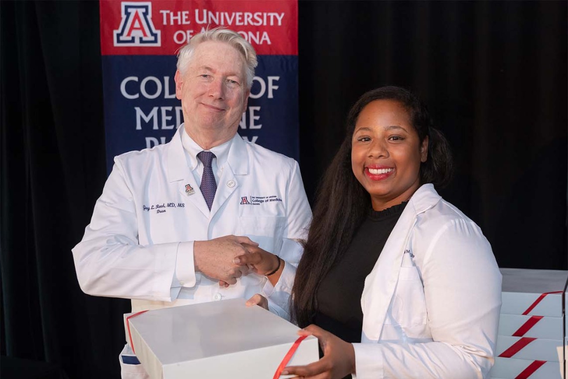 Dean Guy Reed, MD, MS, presents Jade Parker-Character with a box containing medical scrubs during the ceremony.