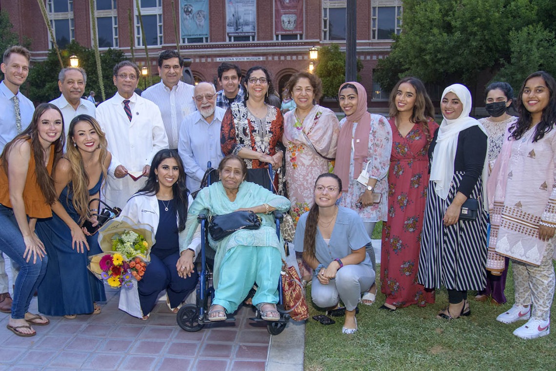 UArizona College of Medicine – Tucson’s Duri Sabina Saeed, kneeling with flowers, poses for a photo with her family and friends after the Class of 2025 white coat ceremony at Centennial Hall.