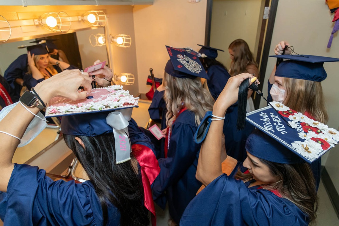 Graduates arrange their highly decorated graduation caps before the start of the college’s August commencement ceremony.