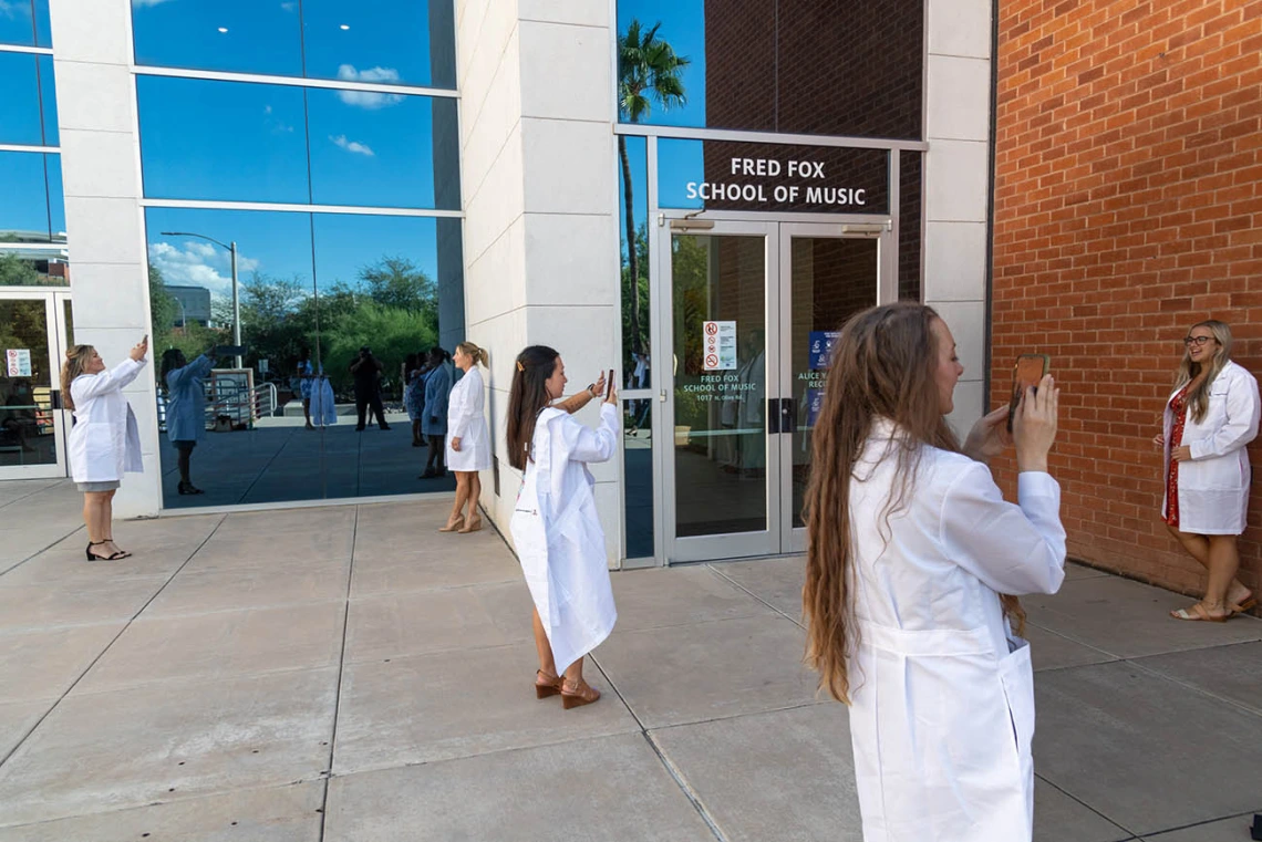 Newly white-coated Doctor of Nursing Practice students take photos of each other after their ceremony ended. 