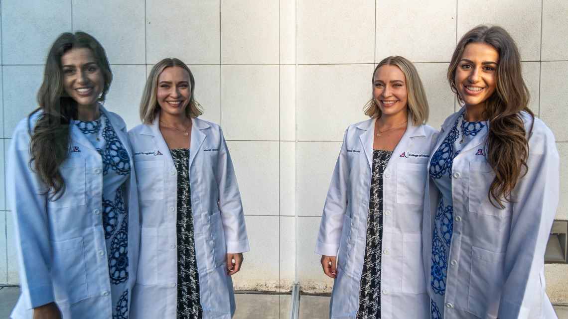 Danielle Crooke and Sarah Bricker (dark hair) are reflected in a window outside of Crowder Hall after their Doctor of Nursing Practice white coat ceremony. 