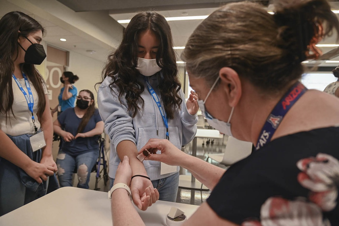 Colette Scott, director of Interprofessional Clinical and Professional Skills Center, right, uses makeup to create a bruising affect on ACES camper Isabella Espinoza. The campers then went into their clinical practice presenting with bruising. 