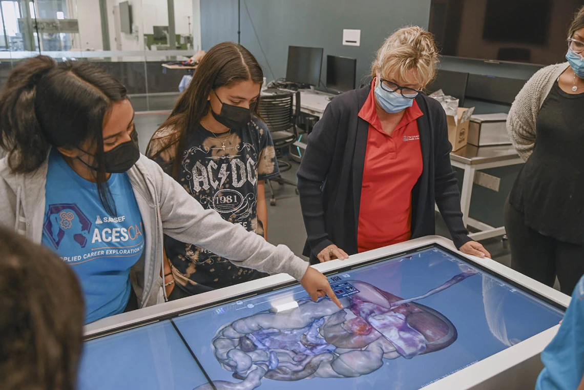 ASTEC’s Deana Ann Smith, RN, (second from right) shows students the Anatomage table in the ASTEC lab, where students practiced dissecting a digital body. 