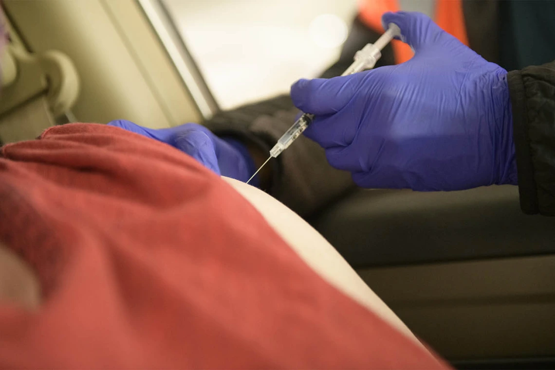 Kerry Johnson administers the COVID-19 vaccine while the recipient remains in their vehicle.