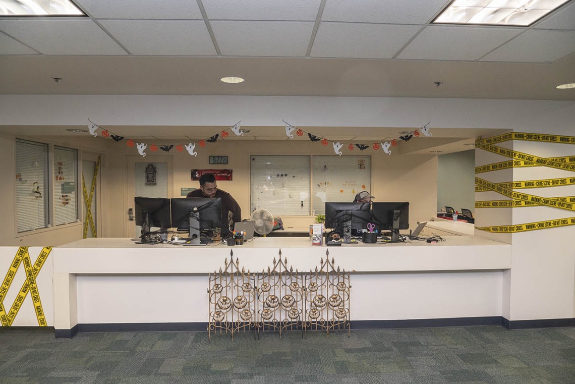 A wide reception desk with Halloween decorations all around it, including yellow caution tape, little ghosts hanging from the ceiling. 