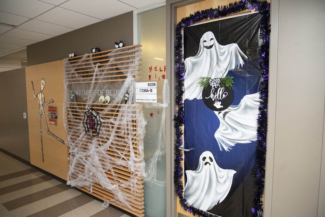Hallway with spider webs and other Halloween decorations on the walls and ghosts on a door. 