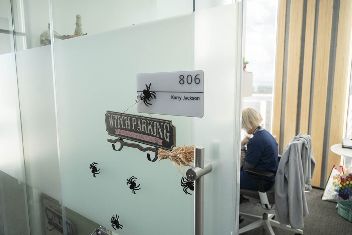 View looking through an open glass office door with a sign that reads, "Witch Parking" with a small witch's broom hanging from it. 