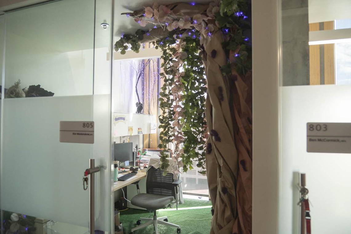 Looking in through a glass office door at a large tree with hanging leaves and various other enchanted forest decorations. 