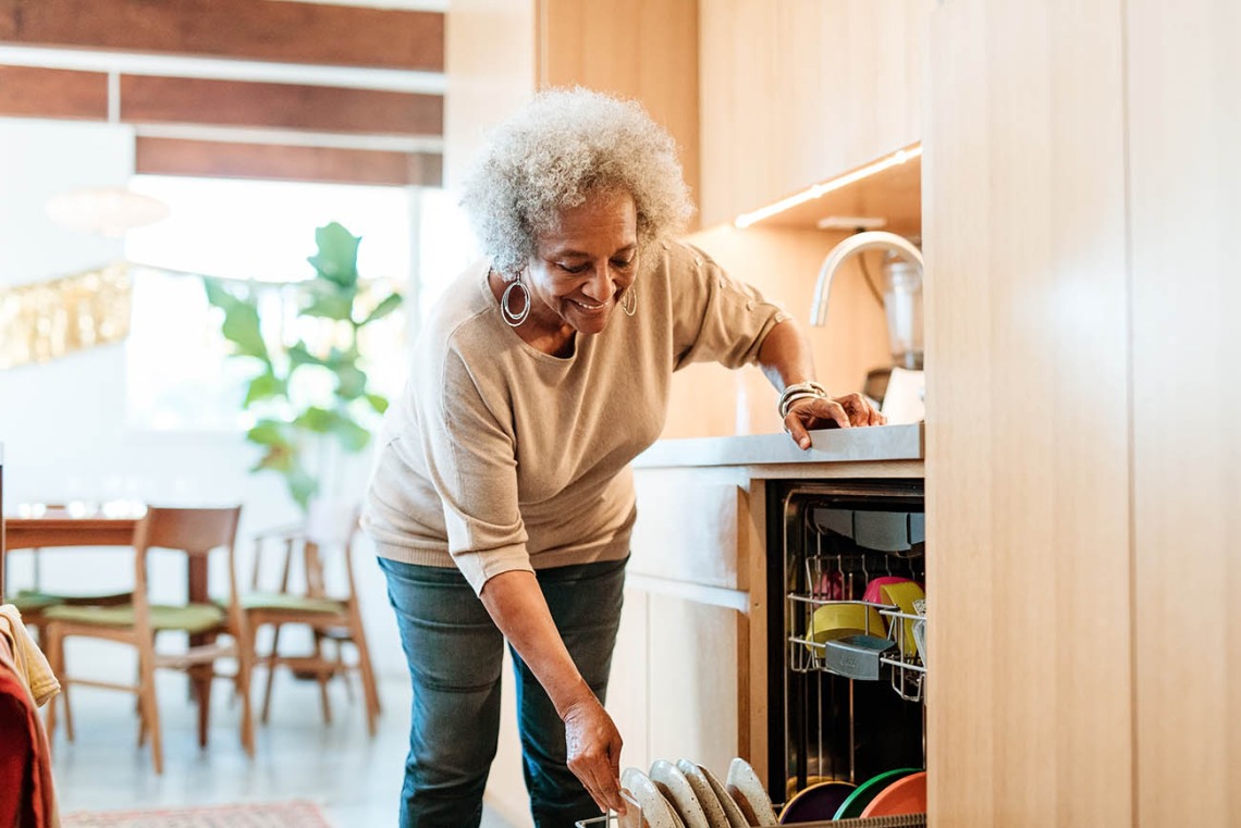 Retired elderly female is doing routine chores in kitchen. 