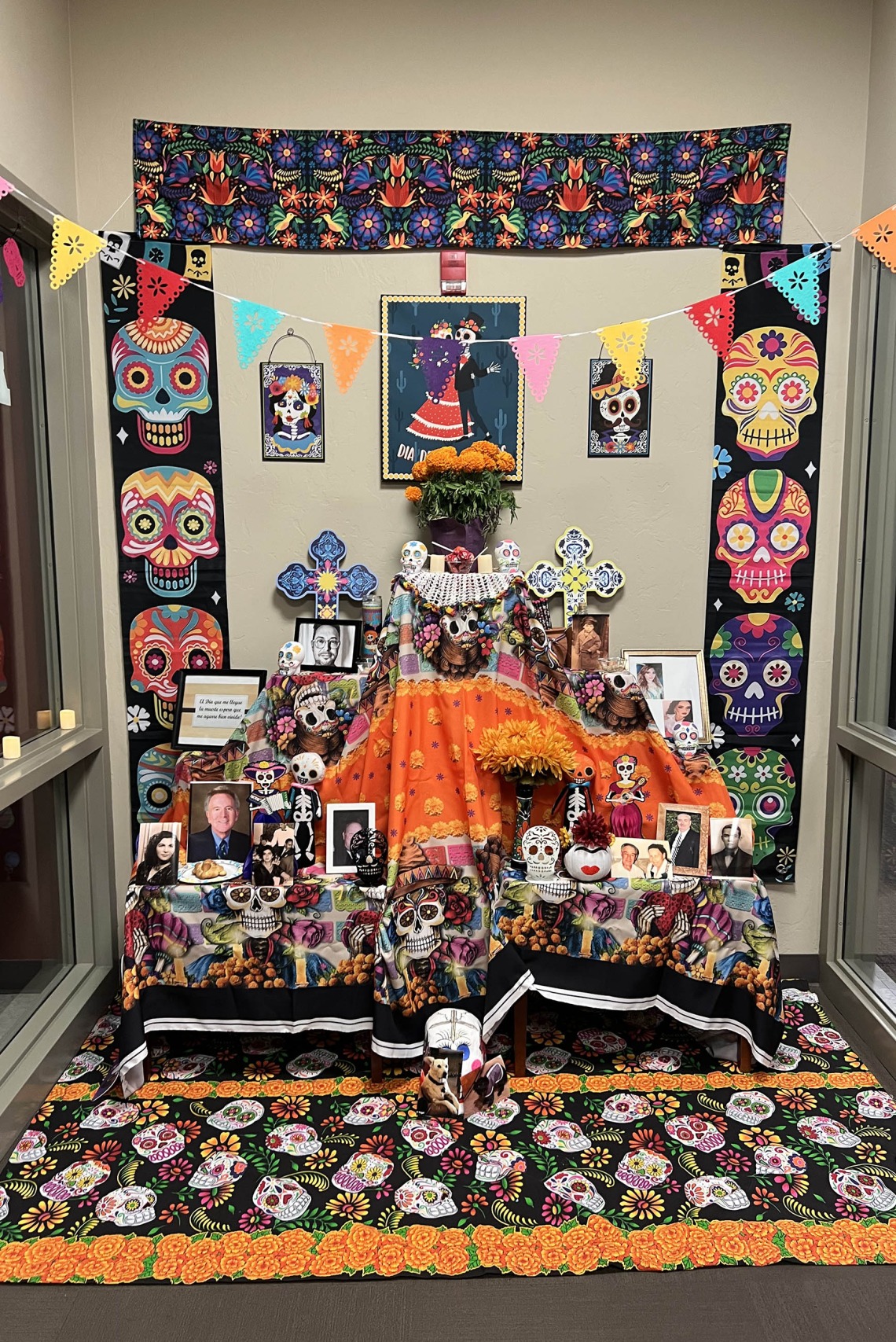 Brightly colored Dia de los Muertos altar with colorful skull design and many photographs on the table. 