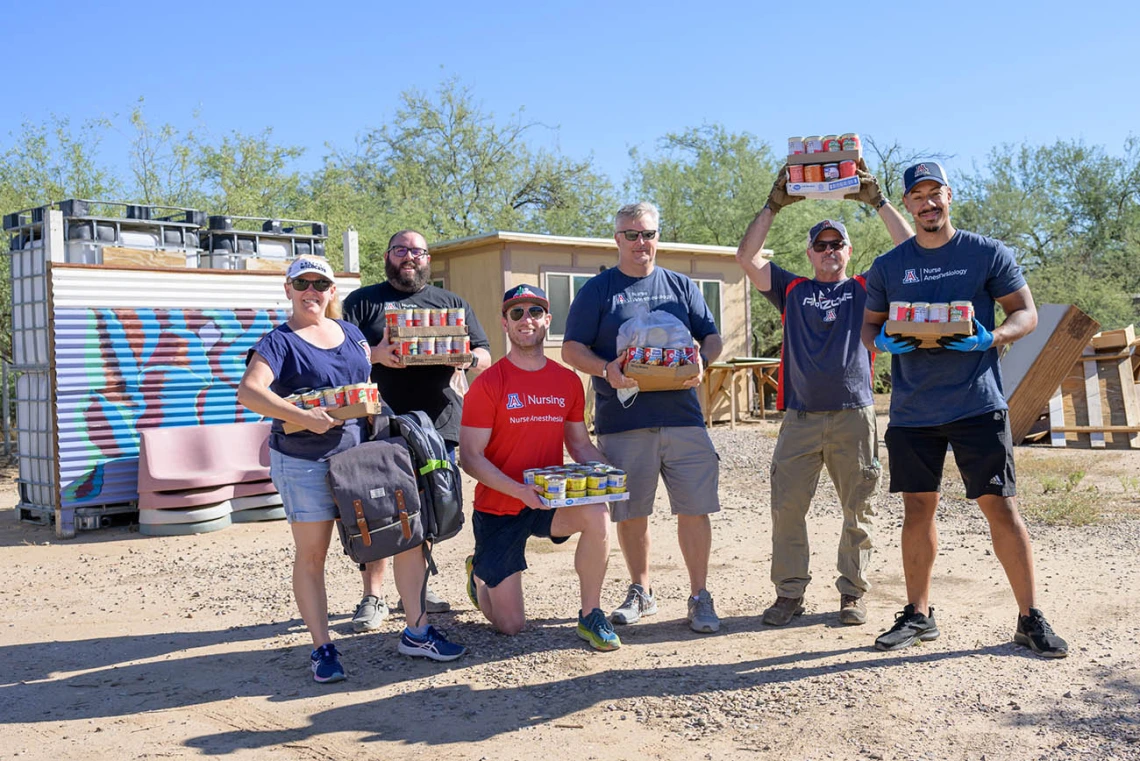 Six faculty and Doctor of Nursing Practice residents stand together outside holding cases of food and supplies to donate. 