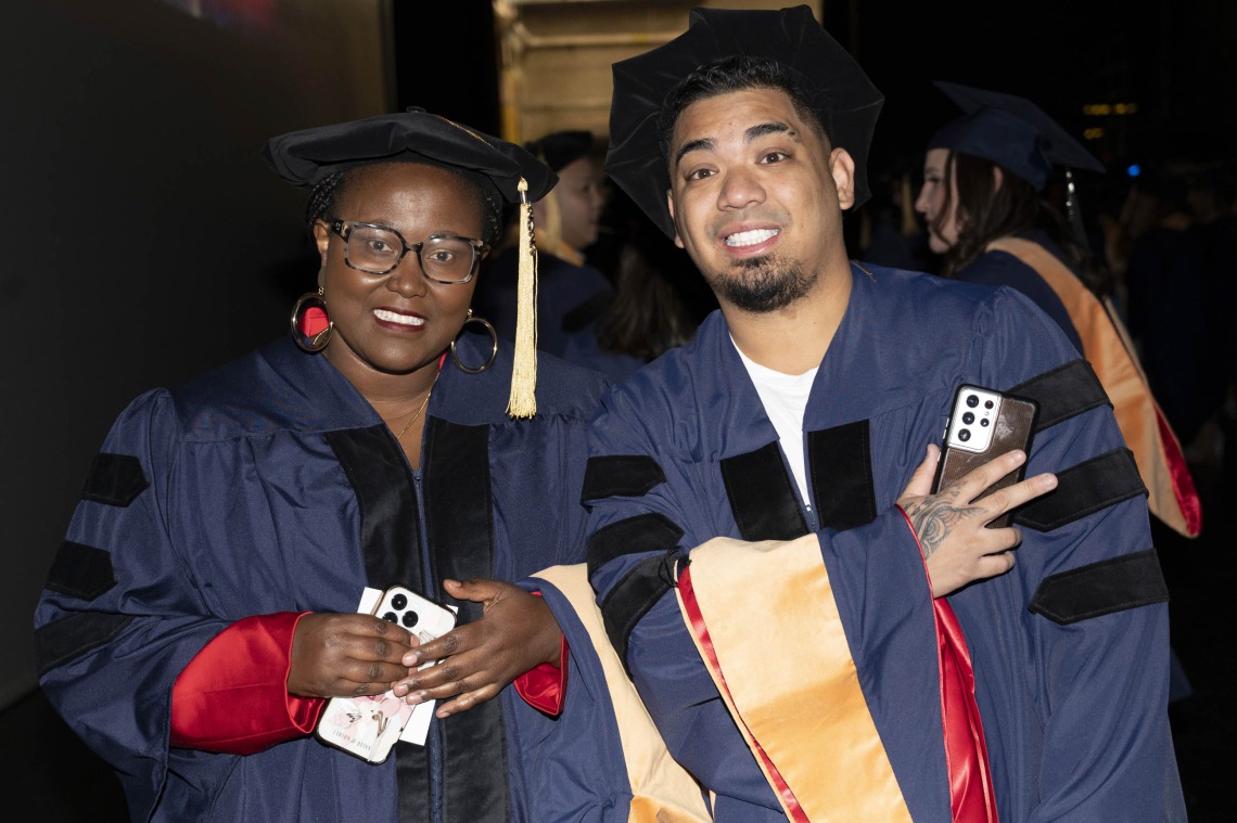 Two smiling nursing students in caps and gowns stand together. 