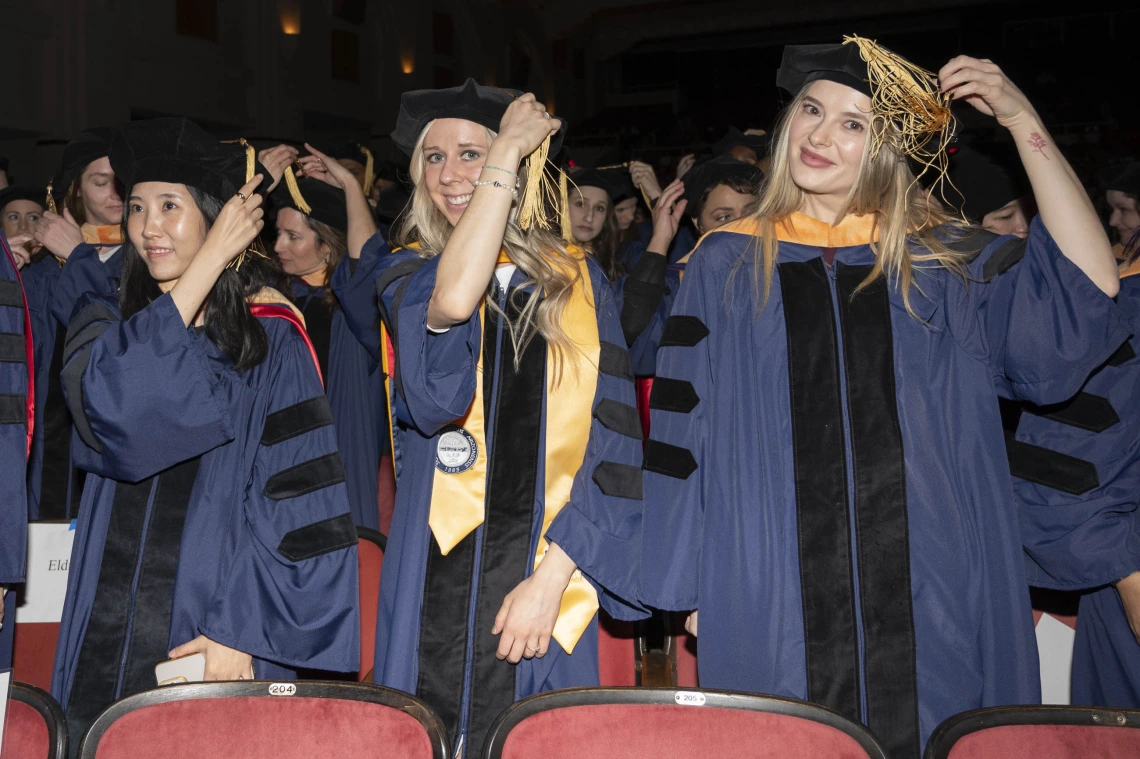 Several nursing graduate in caps and gowns move the tassels on their caps from one side to the other. 