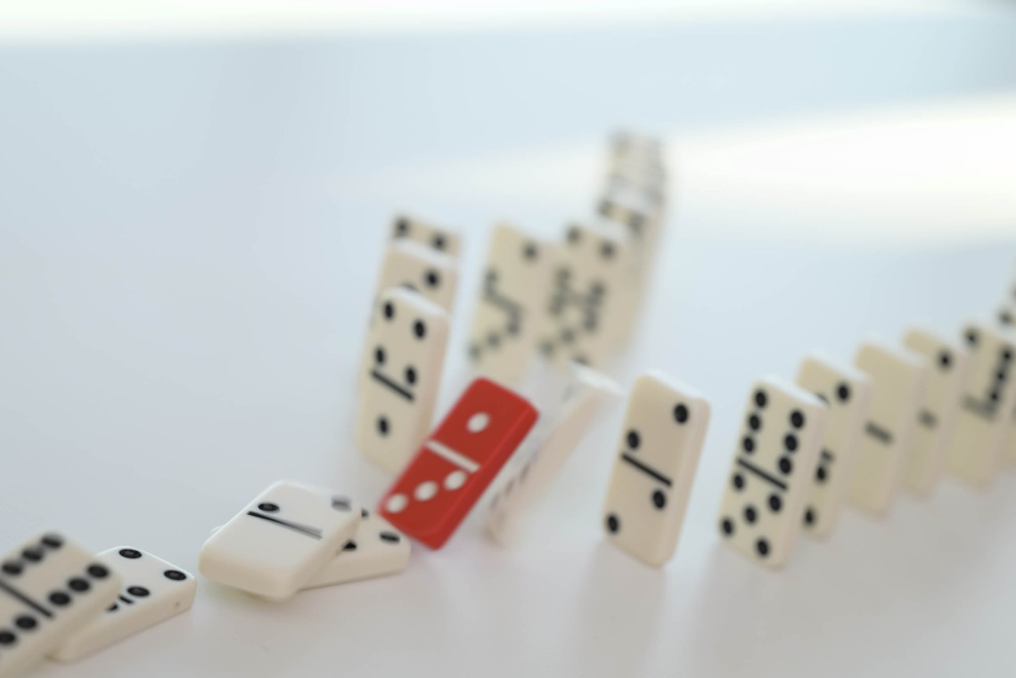 A line of white dominoes with a red domino in the middle representing a gene mutation