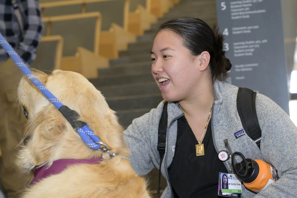 A woman smiles as she pets a golden retriever. 