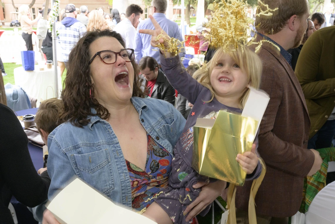 A child tosses crinkle paper into the air from a box while being held by her mom, a fourth-year medical student at the University of Arizona College of Medicine – Tucson, during the Match Day ceremony. 