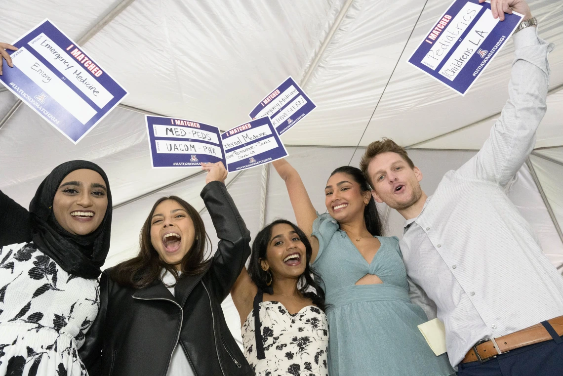 Five College of Medicine – Tucson fourth-year medical students hold up small signs in celebration after finding out where they matched for residency. 