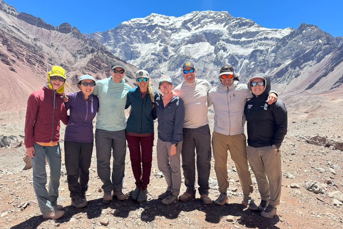 A line of eight men and women stand smiling in front of Aconccagua.