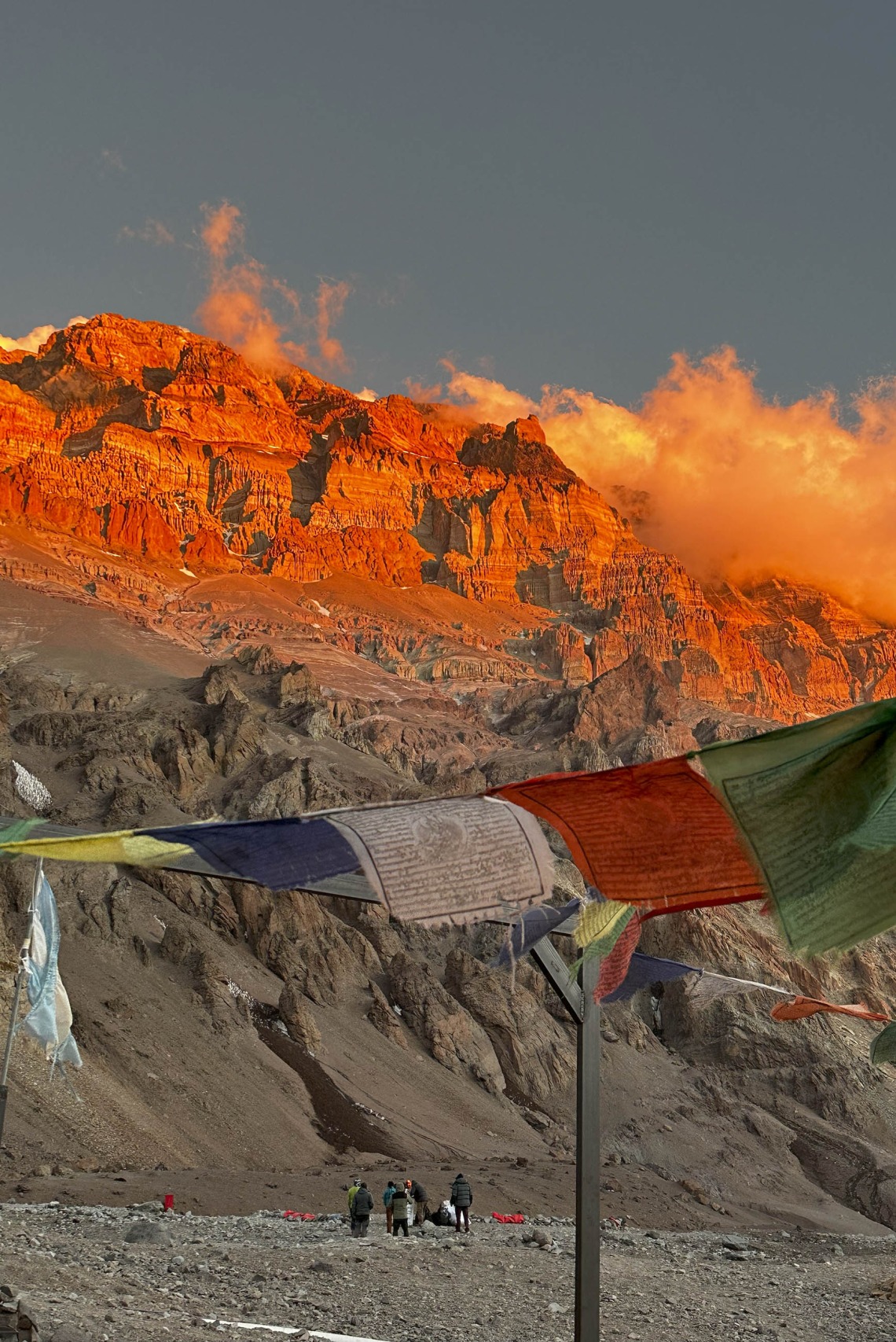 Prayer flags flutter in the wind with mountains and clouds looming in the background.