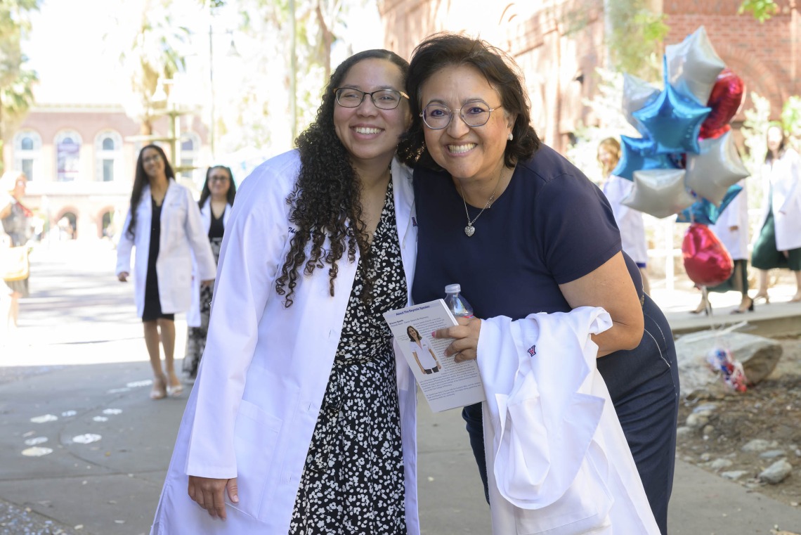 A pharmacy student smiles while standing with a professor outside after leaving the University of Arizona R. Ken Coit College of Pharmacy white coat ceremony. 