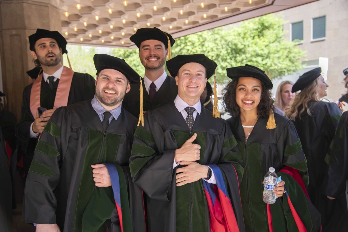 Five University of Arizona College of Medicine – Phoenix students dressed in graduation regalia stand together smiling before their commencement ceremony.