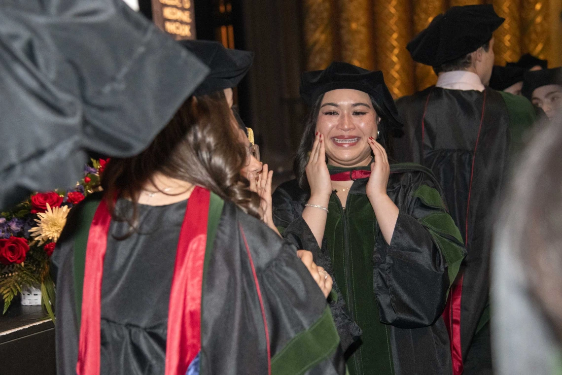 A University of Arizona College of Medicine – Phoenix student in graduation regalia holds her hands to her face as she smiles at the conclusion of the commencement ceremony.