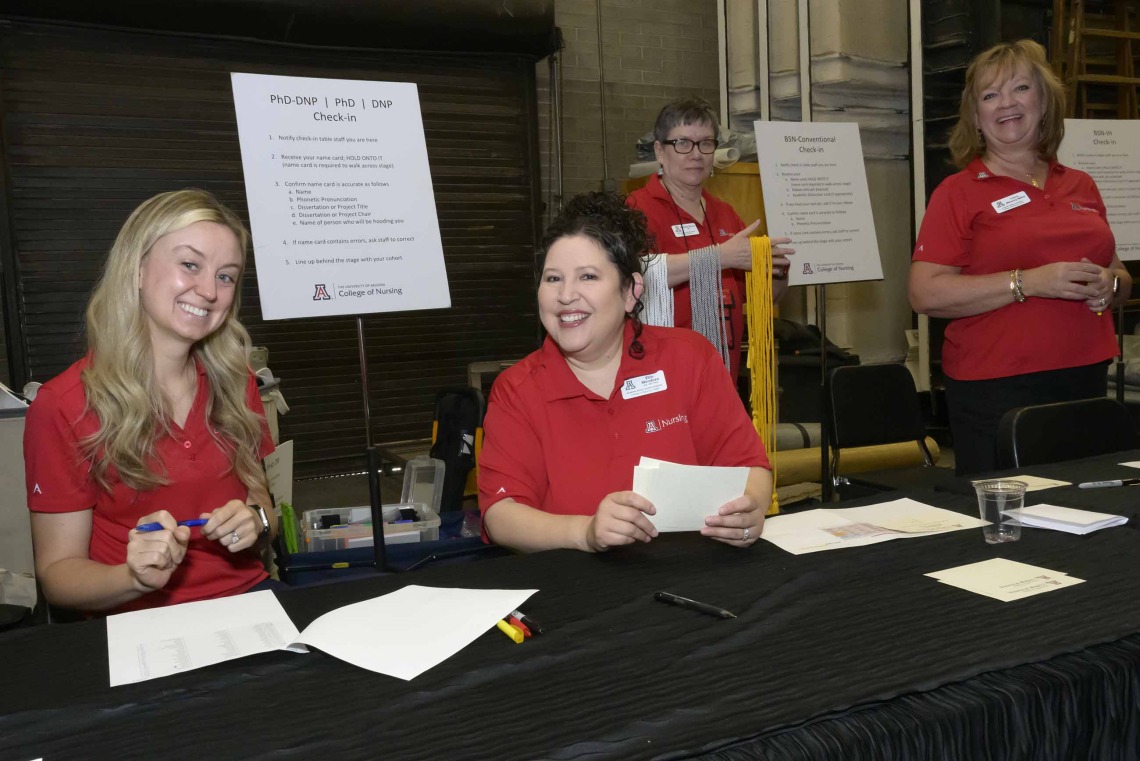 Four University of Arizona College of Nursing staff members work at a check-in table backstage during the convocation ceremony. 