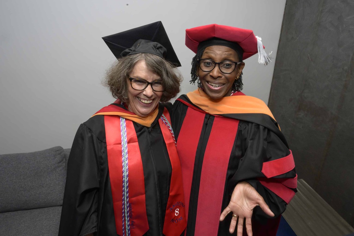 Two University of Arizona College of Nursing faculty members in graduation caps and gowns stand together smiling. 