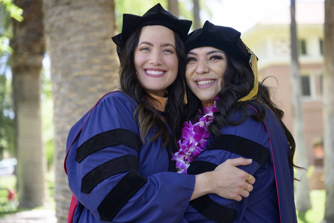 Two University of Arizona College of Nursing graduates in caps and gowns smile as they hug. 