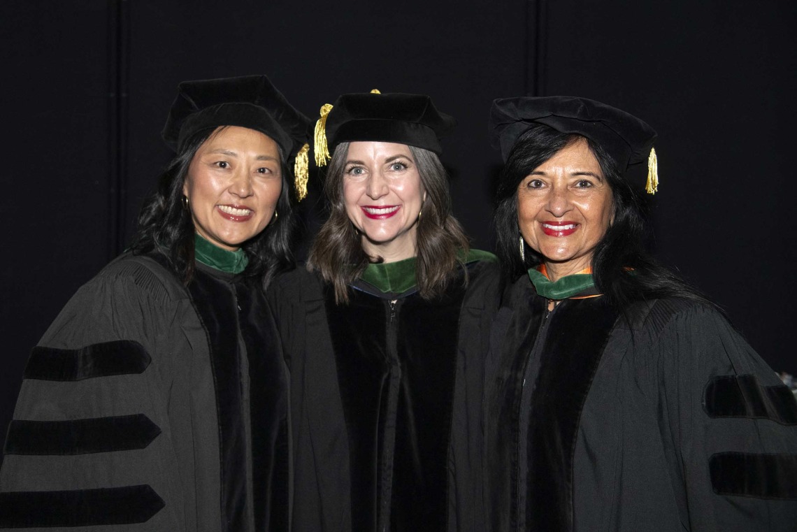 Three University of Arizona College of Medicine – Tucson professors in graduation caps and gowns stand together, smiling.  