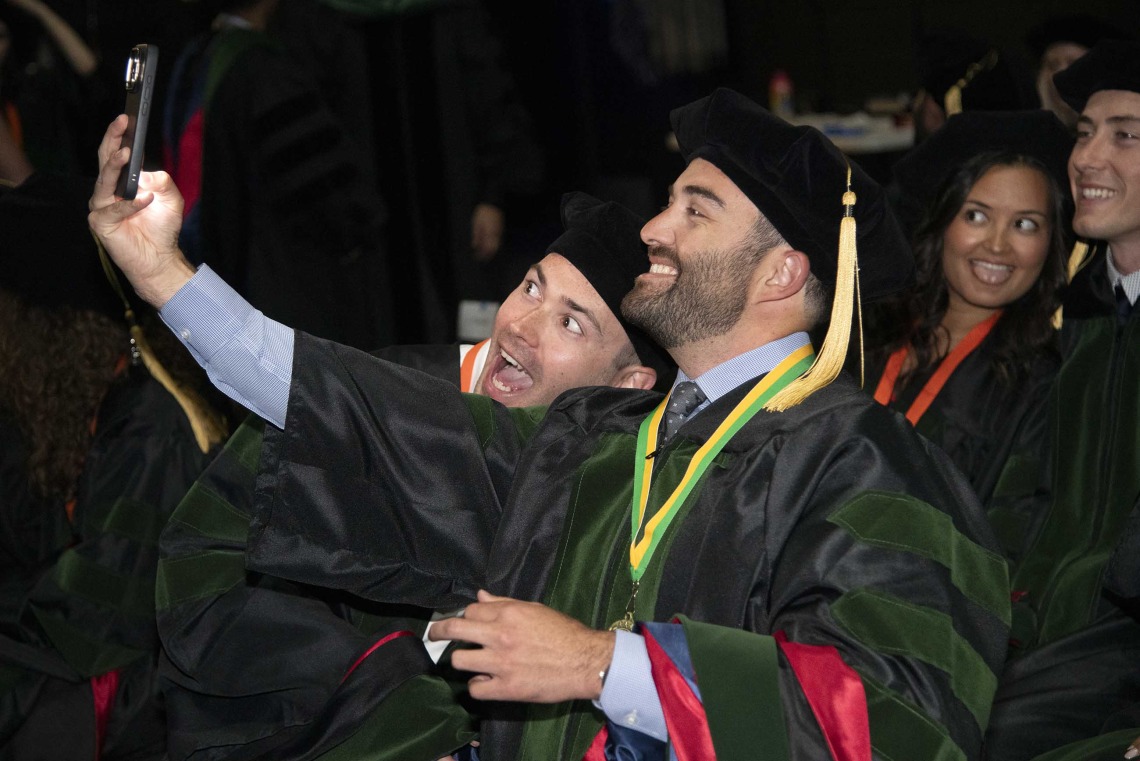 Two University of Arizona College of Medicine – Tucson students in graduation regalia take a selfie before their graduation ceremony. 
