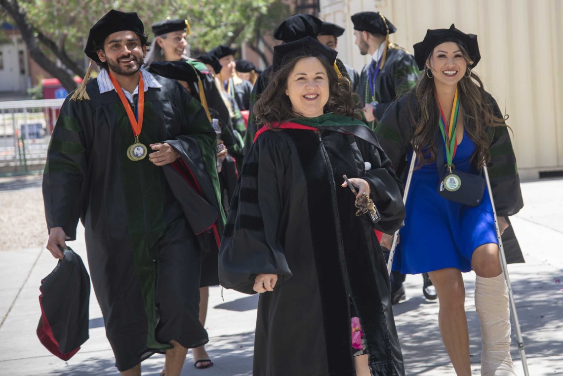 Faculty and students from the University of Arizona College of Medicine – Tucson, dressed in graduation caps and gowns, walk outside on their way to the commencement ceremony. 