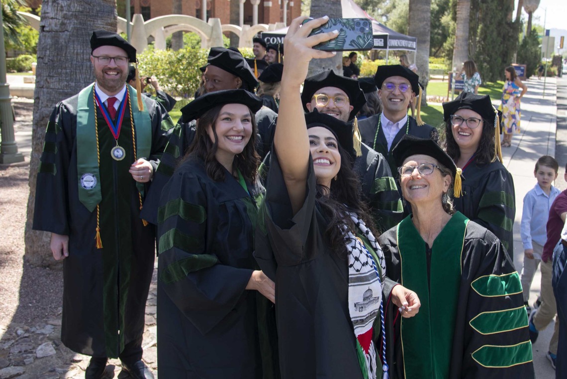 Students from the University of Arizona College of Medicine – Tucson, dressed in graduation caps and gowns, take a selfie outside on their way to the commencement ceremony.