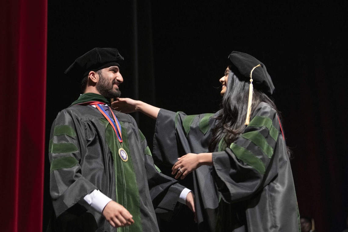 Two people dressed in caps and gowns reach for each other to hug during the University of Arizona College of Medicine – Tucson graduation ceremony. 