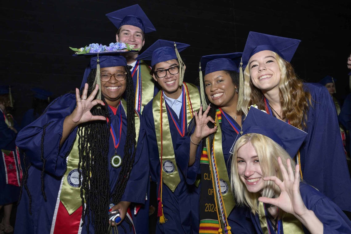 Six University of Arizona R. Ken Coit College of Pharmacy students dressed in graduation caps and gowns show the “Wildcat” hand sign while smiling. 
