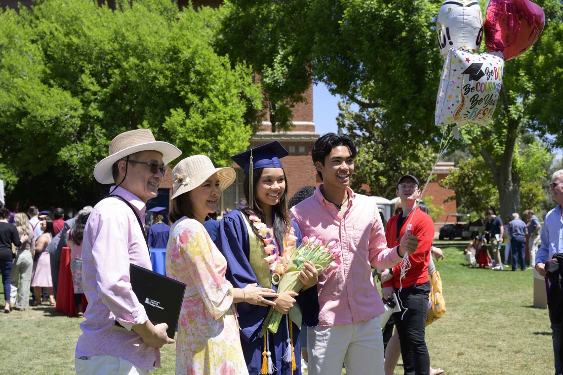 A University of Arizona R. Ken Coit College of Pharmacy graduate wearing a cap and gown holds flowers while standing with her parents and brother. 
