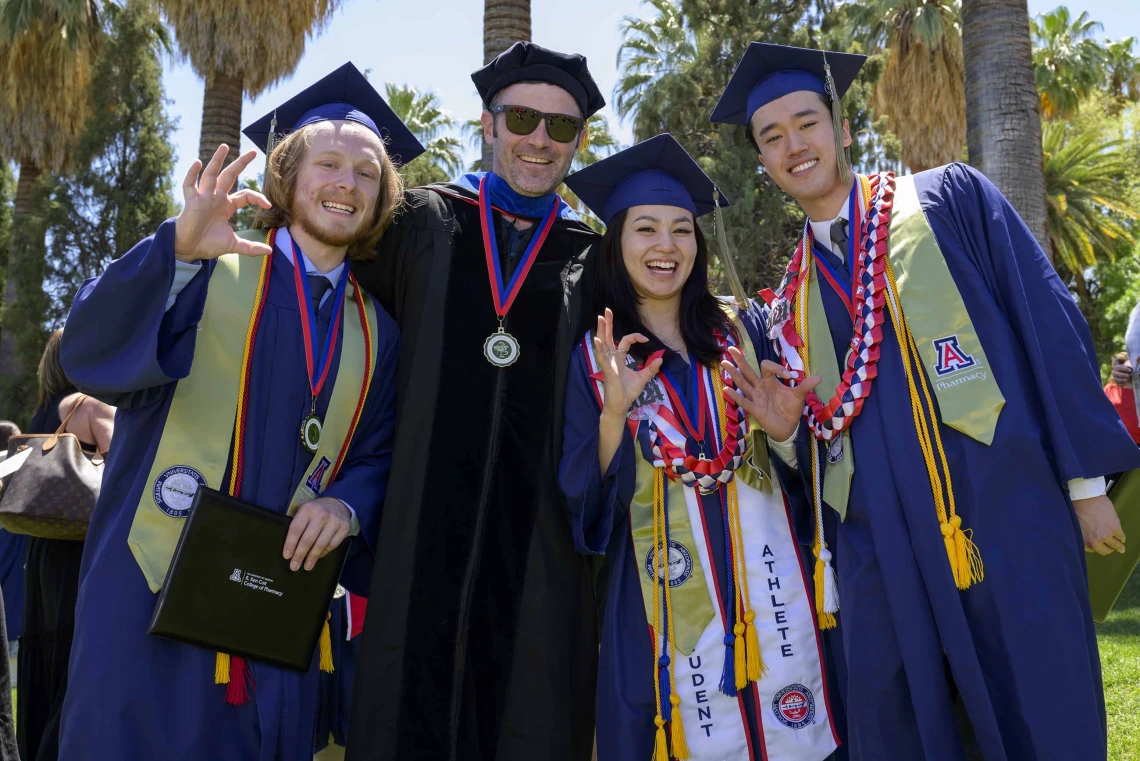 Three University of Arizona R. Ken Coit College of Pharmacy students and one faculty member, all dressed in graduation caps and gowns, stand side by side, smiling. 