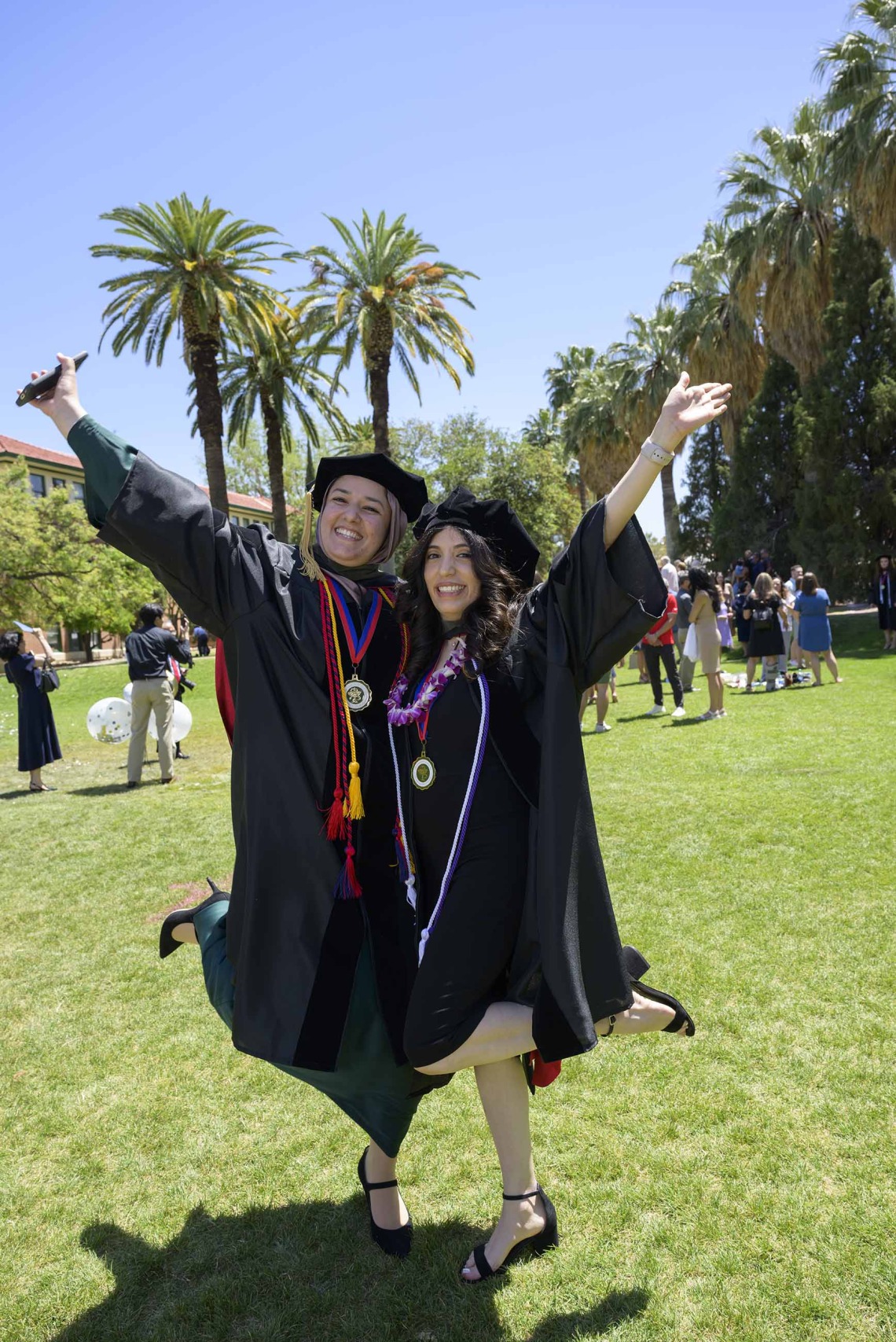 Two University of Arizona R. Ken Coit College of Pharmacy students wearing graduation caps and gowns celebrate with their hands in the air.