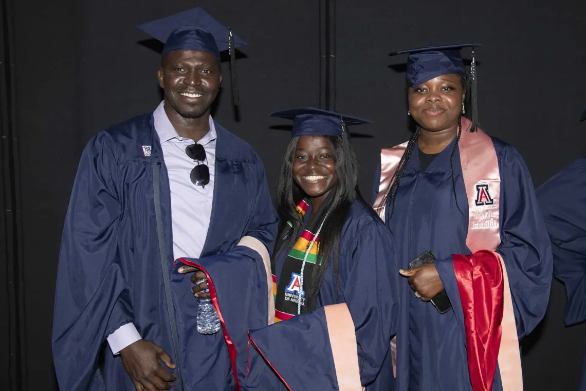 Three University of Arizona Mel and Enid Zuckerman College of Public Health students, all wearing graduation caps and gowns, stand next to each other and smile.