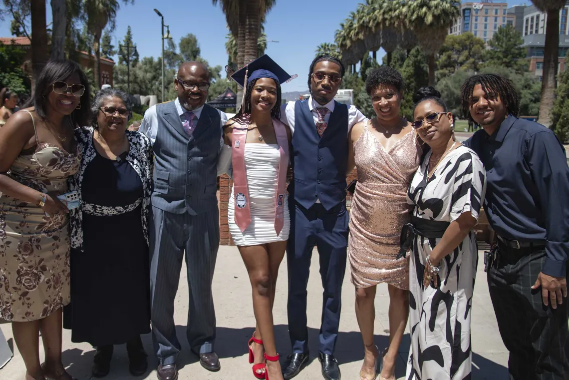 A University of Arizona Mel and Enid Zuckerman College of Public Health student wearing a graduation cap and stole stands with several members of her family outside.