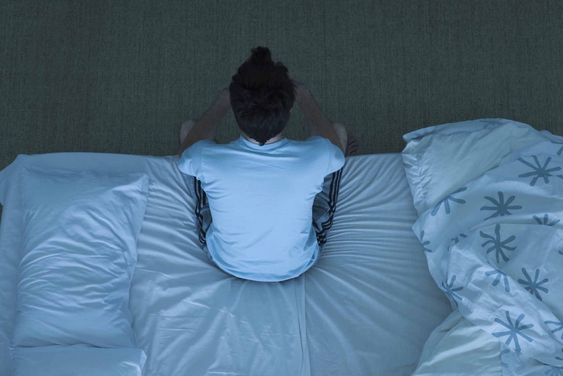 person sitting on edge of bed at night, unable to sleep