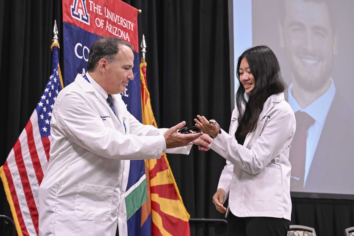 University of Arizona College of Medicine – Phoenix Dean Fred Wondisford presents a stethoscope to a new medical student. Both are wearing white medical coats. 
