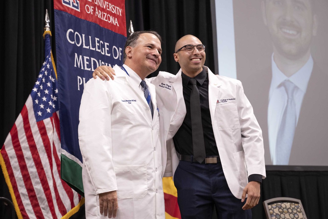 University of Arizona College of Medicine – Phoenix Dean Fred Wondisford poses for a photo with a new medical student. Both are wearing white medical coats.
