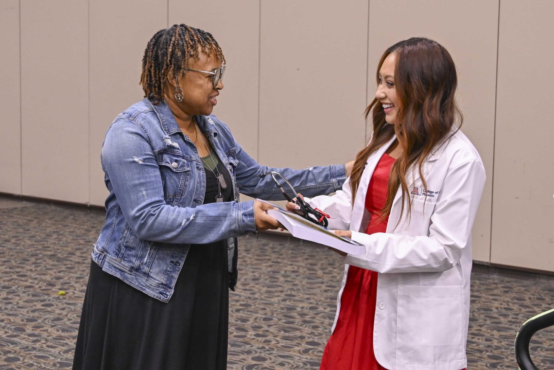 A University of Arizona College of Medicine – Phoenix staff member hands a book to a new medical student. Both are smiling. 