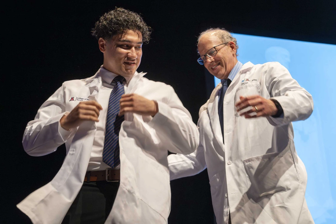 A University of Arizona College of Medicine – Tucson student adjusts a medical white coat that was just put on him by a professor.