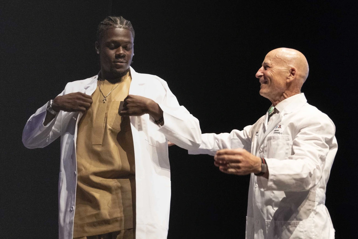 A University of Arizona College of Medicine – Tucson student adjusts a medical white coat that was just put on him by a professor.