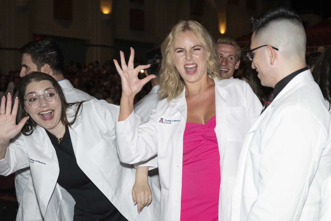 Several incoming University of Arizona College of Medicine – Tucson students wearing medical white coats wave, smile and flash the Arizona Wildcats hand sign. 