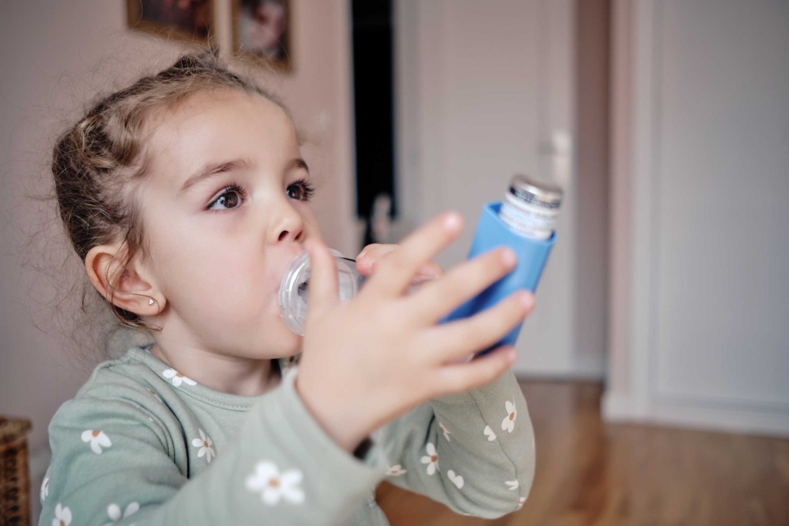 Young child using inhaler with a spacer device.