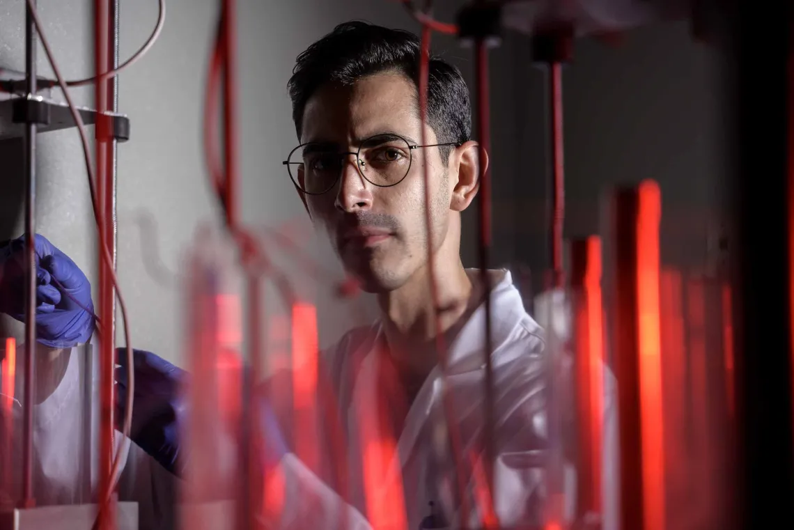 Portrait of research scientist Robson Vizin looking through red lab tubes. 