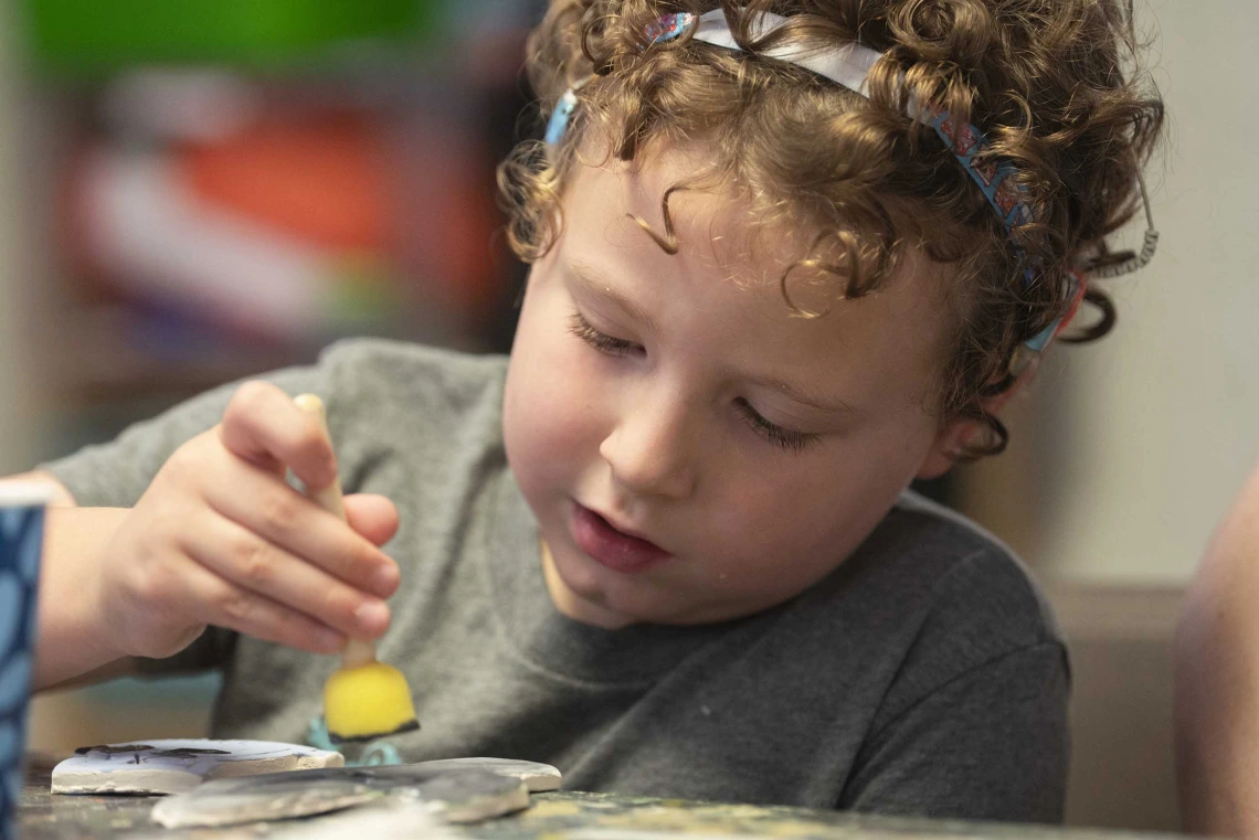 A young girl focuses intently as she paints an art project. 